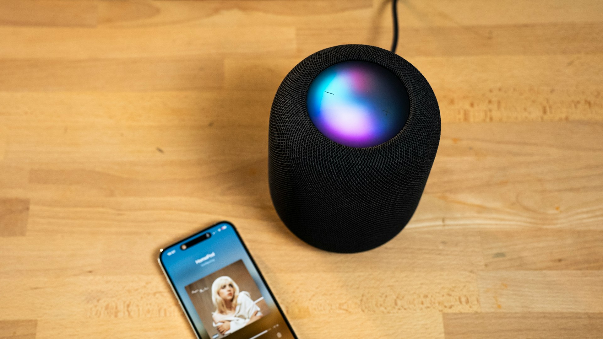 a smart speaker next to an iphone on a wooden table